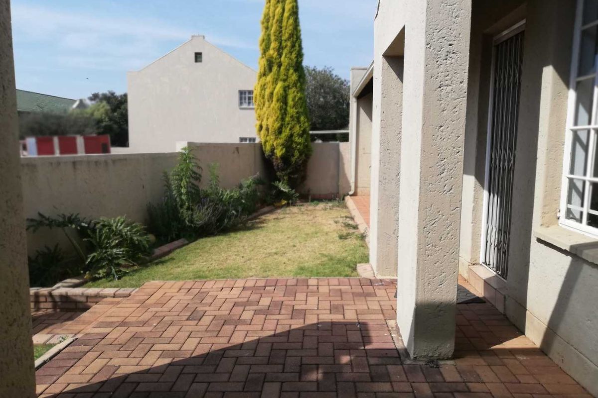 A private rear courtyard featuring a paved patio area, a small lawn, and perimeter boundary walls.
