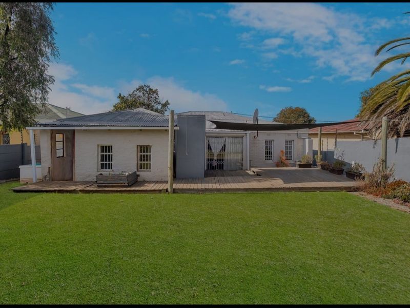 Rear view of the property featuring a spacious lawn, timber decking, and a shade sail, providing a functional outdoor entertainment area.