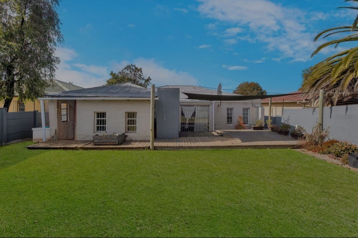 Rear view of the property featuring a spacious lawn, timber decking, and a shade sail, providing a functional outdoor entertainment area.