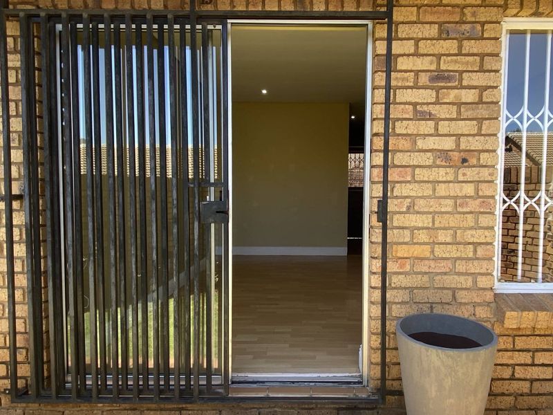 Exterior view of a townhouse entrance featuring a security gate, sliding door access, and brick facade with window security bars.