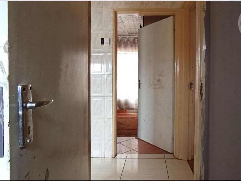 A view through a doorway into a tiled hallway, showing basic finishes and internal door access to adjacent rooms.