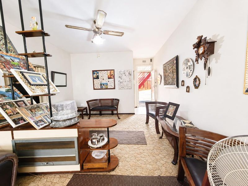 A living room area featuring a ceiling fan and built-in shelving unit, with dated carpet flooring throughout the space.