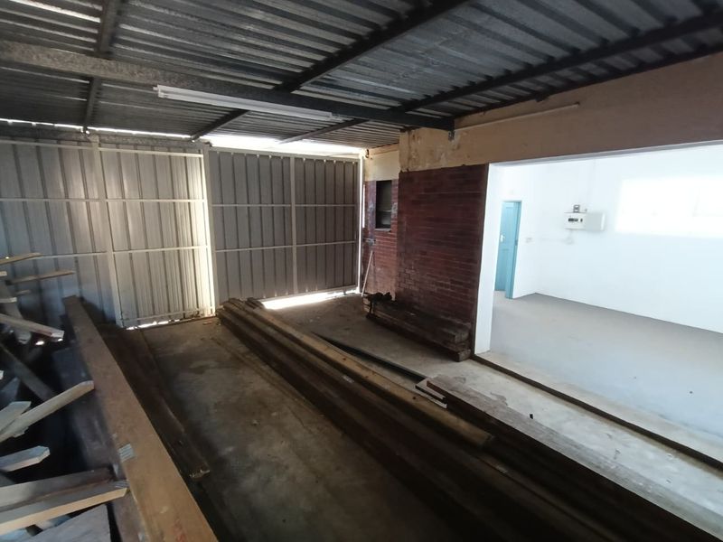 Spacious industrial garage area featuring exposed brickwork, corrugated metal roofing, and concrete flooring, suitable for storage or workshop use.
