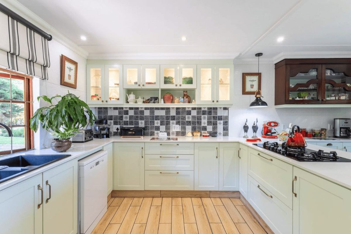 A well-maintained U-shaped kitchen featuring light green cabinetry, stone countertops, a tiled backsplash, and integrated gas hob with extractor fan.