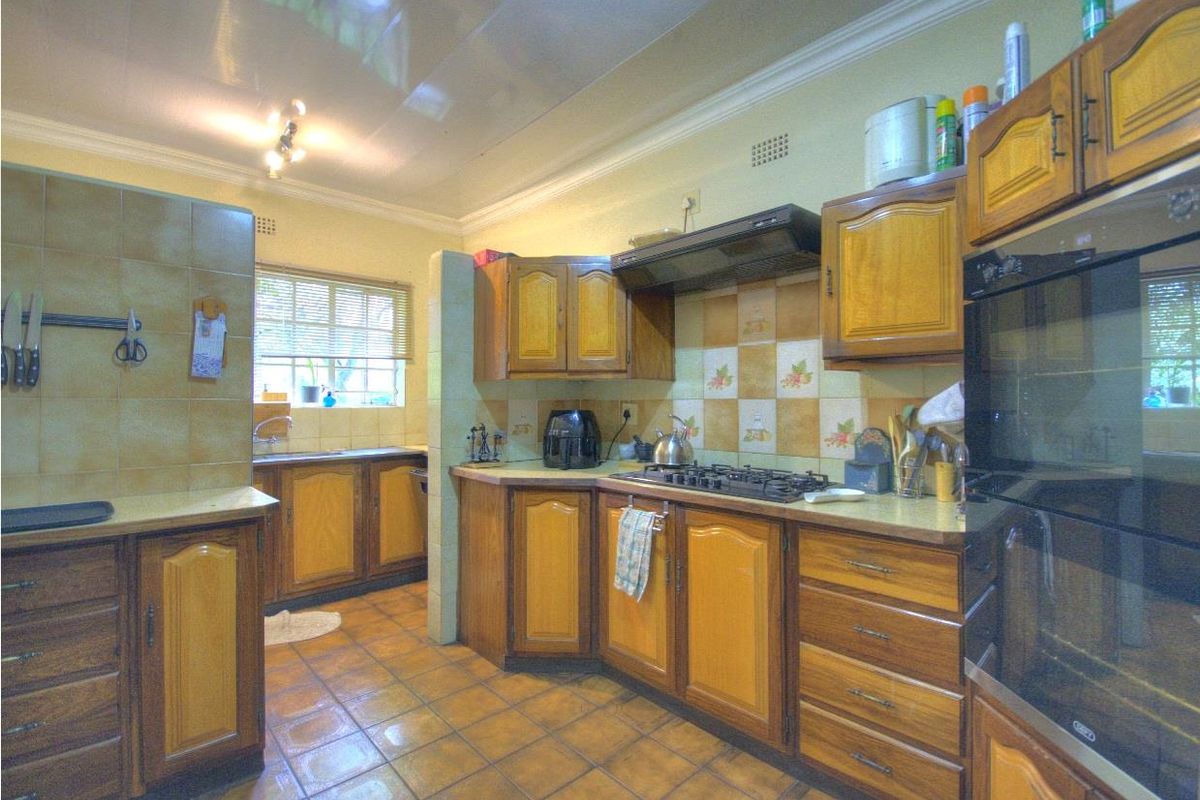 A functional kitchen featuring wooden cabinetry, built-in oven, gas hob, extractor fan, and tiled flooring with a separate wash-up area.