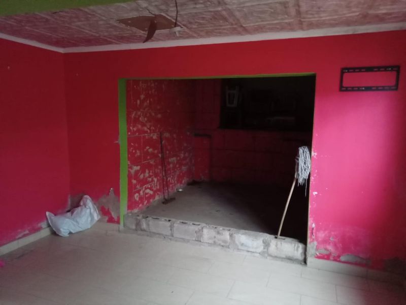 An empty living area featuring a raised platform and textured ceiling, currently requiring significant wall repairs and cosmetic renovation to restore the space.