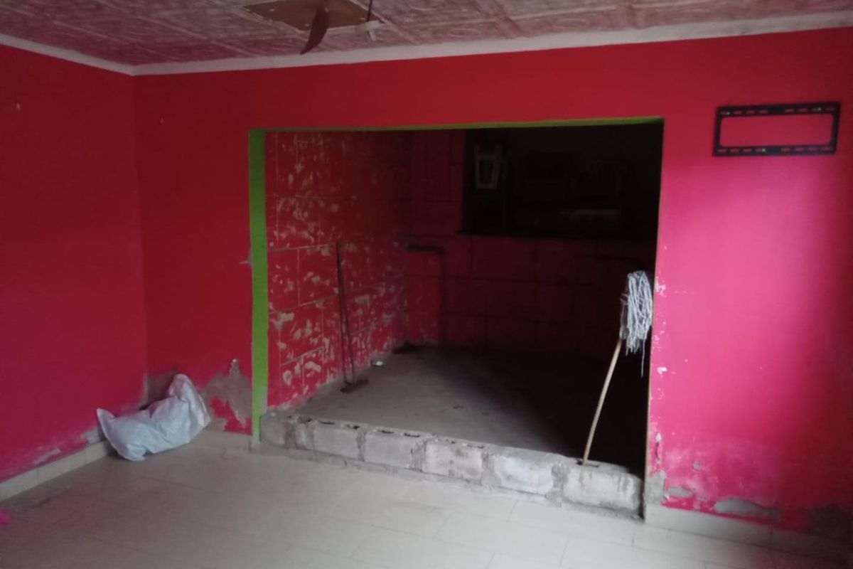 An empty living area featuring a raised platform and textured ceiling, currently requiring significant wall repairs and cosmetic renovation to restore the space.