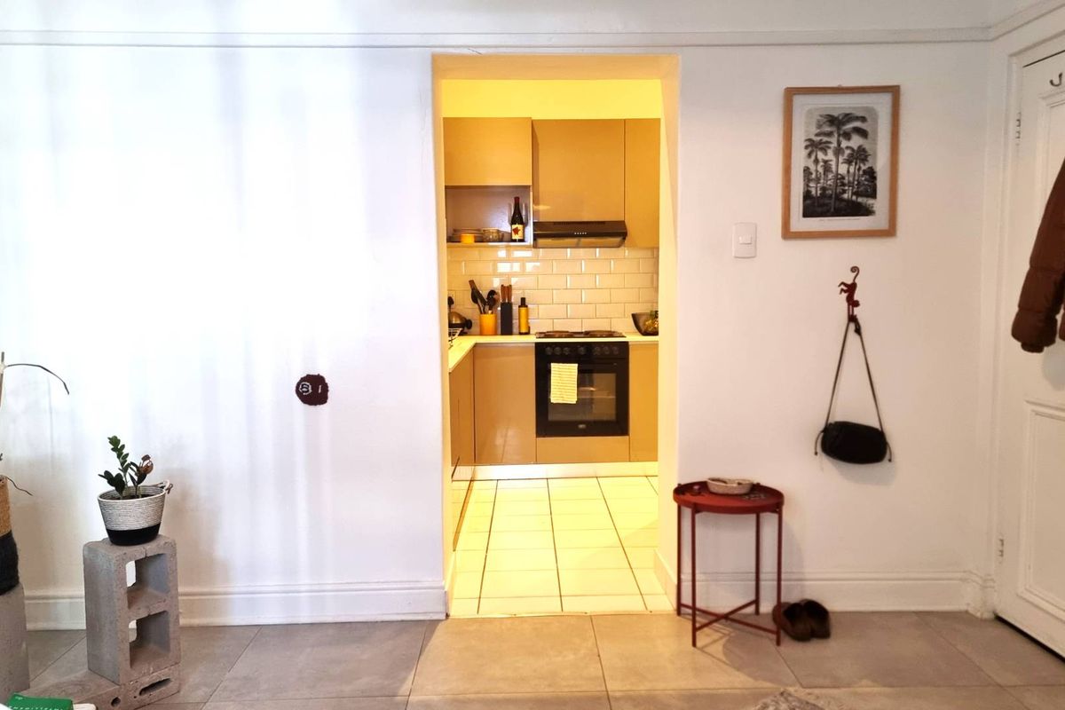 A compact kitchen featuring built-in cabinetry, a subway tile backsplash, and integrated cooking appliances, viewed from an adjacent living area.