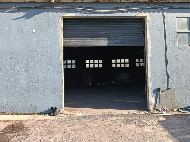 Industrial garage space featuring a large roller shutter door, concrete flooring, and multiple steel-framed windows providing natural light to the interior.