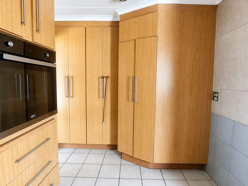 A functional kitchen area featuring light wood-finish cabinetry, a built-in oven, and neutral tiled flooring and splashbacks.