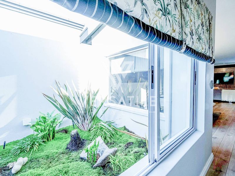 A bright internal courtyard garden feature viewed through a sliding glass door, showcasing a landscaped green space and modern interior flooring.