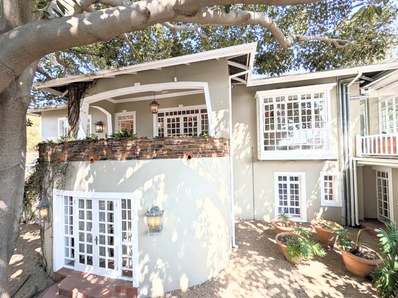 Rear elevation of the house featuring a covered balcony with stone cladding, a prominent bay window, and multiple sets of classic french doors.