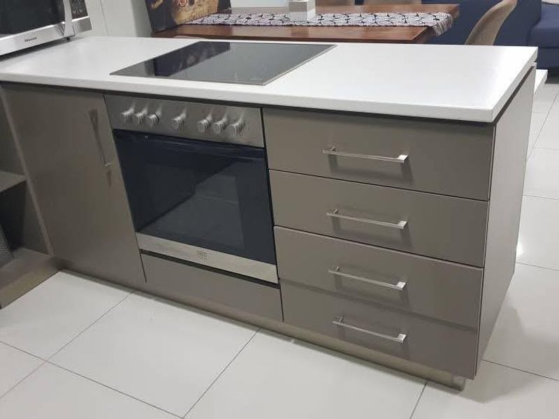 Modern kitchen island featuring a built-in oven, induction cooktop, stone countertops, and sleek cabinetry with tiled flooring.