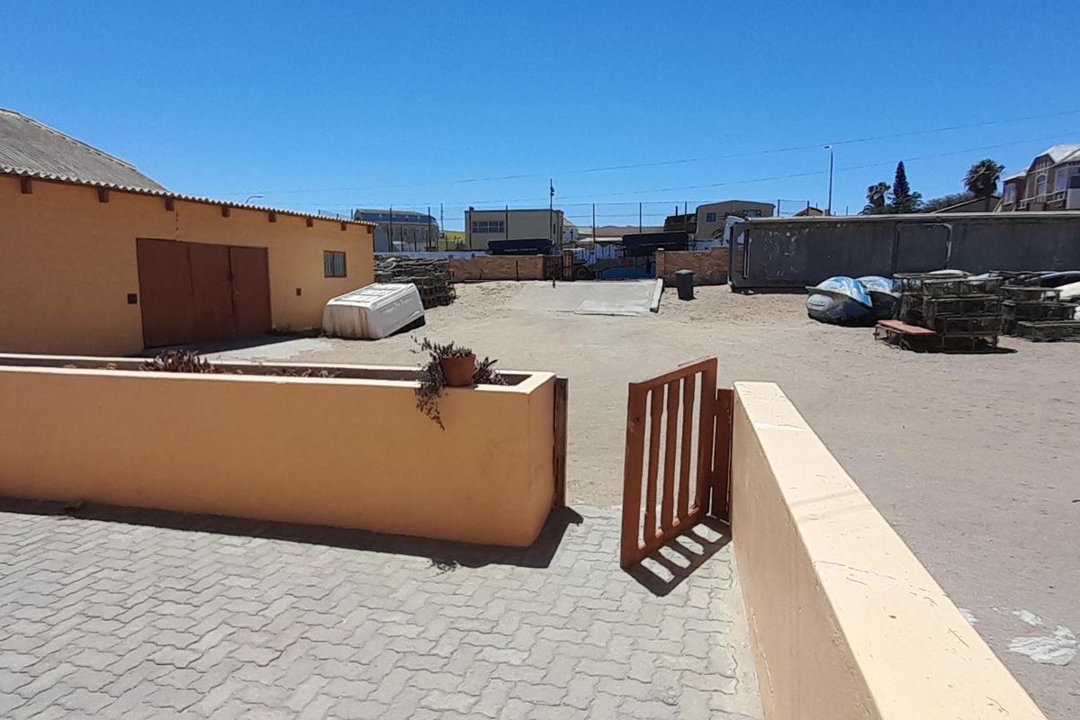 An expansive outdoor area featuring paved sections, low boundary walls, and a large open yard space suitable for storage or development.