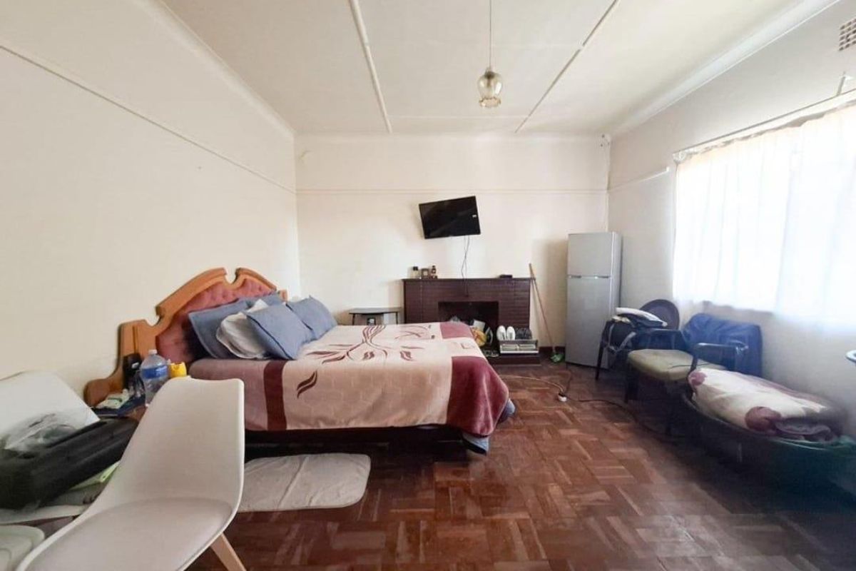 Spacious bedroom featuring original parquet flooring, a built-in brick fireplace, and large windows allowing for natural light.