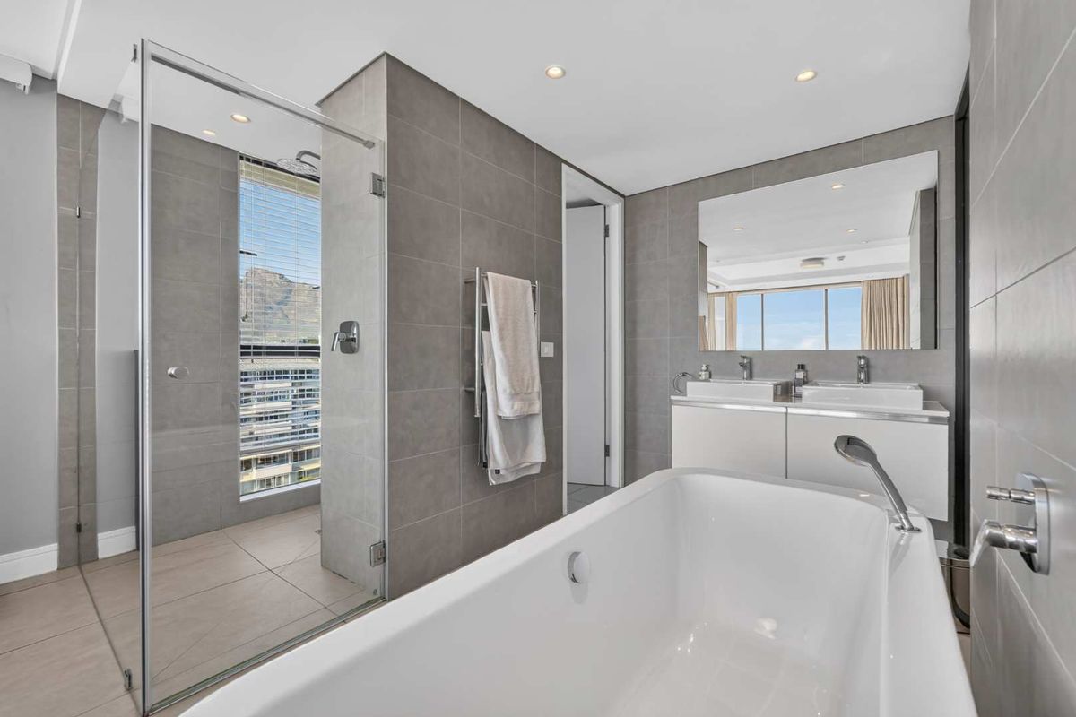 Modern bathroom featuring a freestanding bathtub, glass-enclosed shower, double vanity with integrated sinks, and contemporary grey tiling.