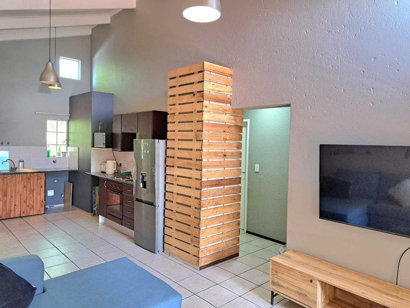 Open-plan living and kitchen area featuring vaulted ceilings, tiled flooring, and functional built-in cabinetry with integrated appliances.