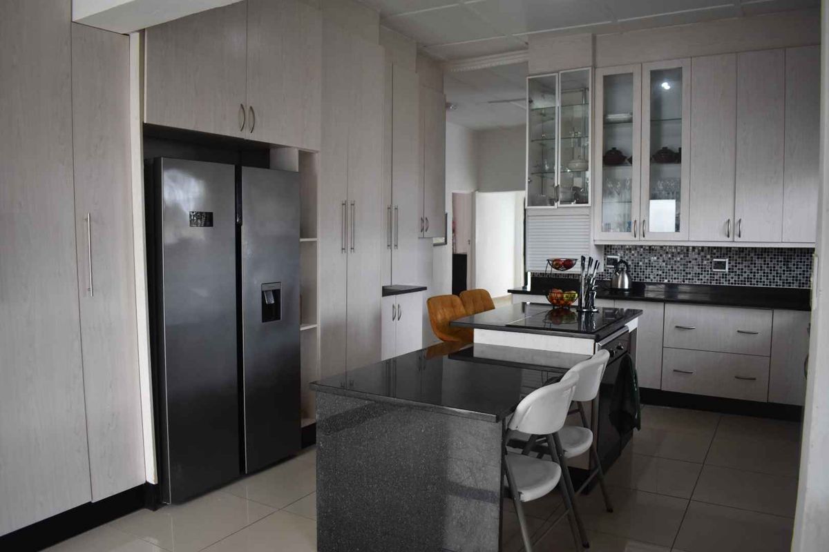 Modern kitchen featuring light-toned cabinetry, dark granite countertops, a central island with breakfast bar seating, and a mosaic tile backsplash.