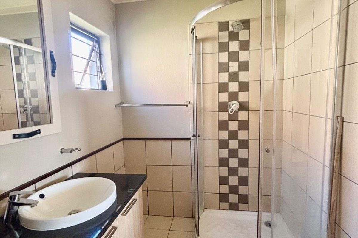 A functional bathroom featuring a curved glass shower enclosure, a vanity cabinet with a countertop basin, and tiled finishes.