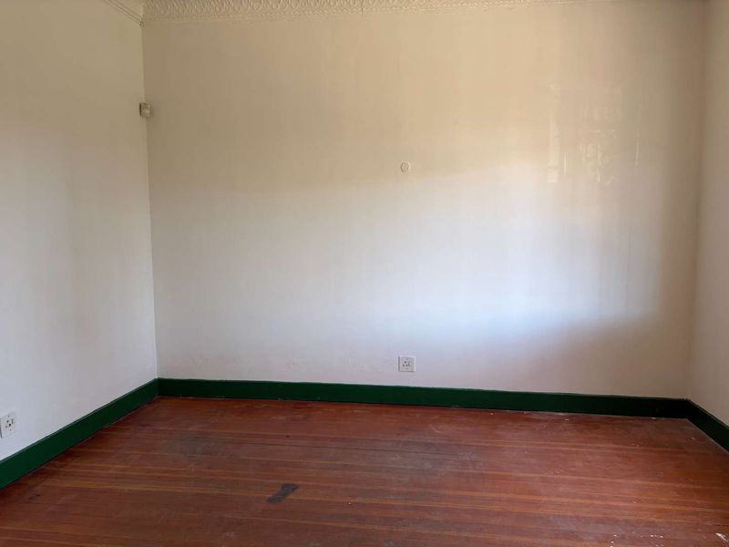 An empty bedroom featuring original hardwood flooring, decorative cornice, and green painted skirting boards, offering a blank canvas for renovation.