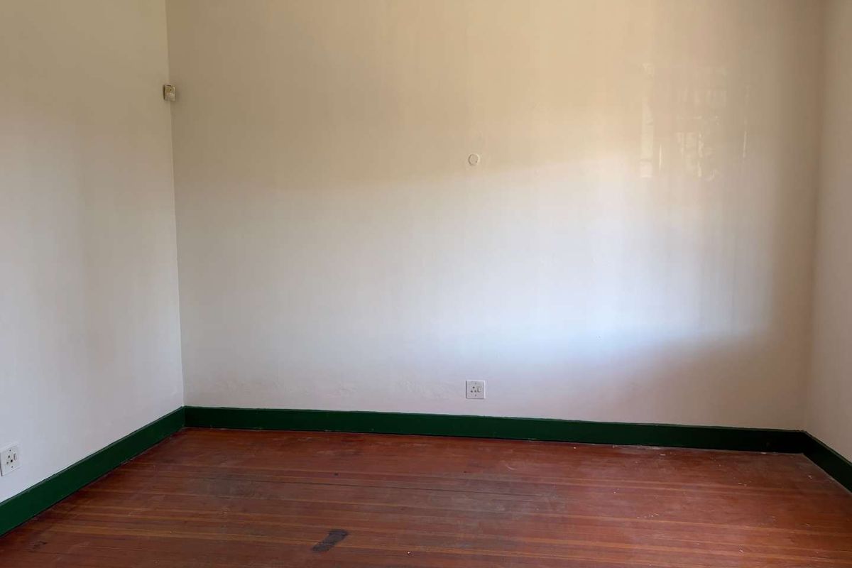 An empty bedroom featuring original hardwood flooring, decorative cornice, and green painted skirting boards, offering a blank canvas for renovation.