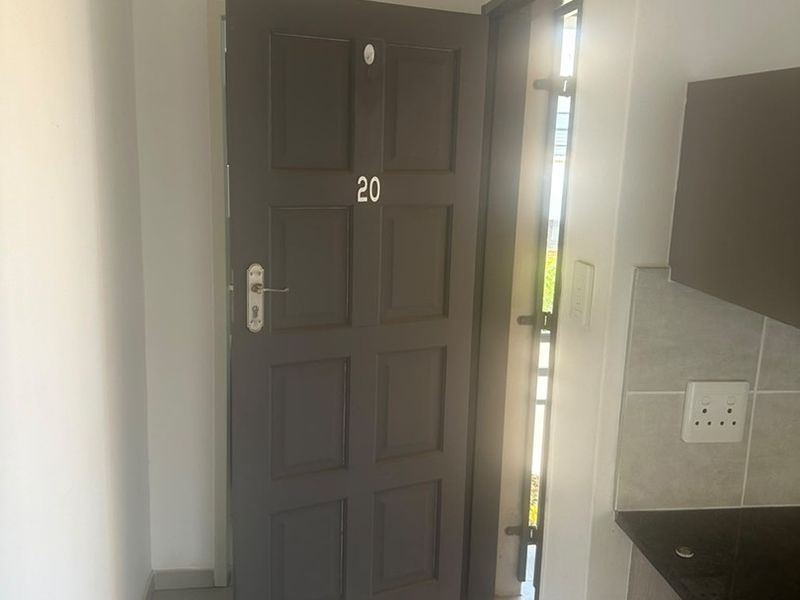 Entrance area featuring a dark grey panelled door, tiled flooring, and adjacent kitchen cabinetry with granite countertops.