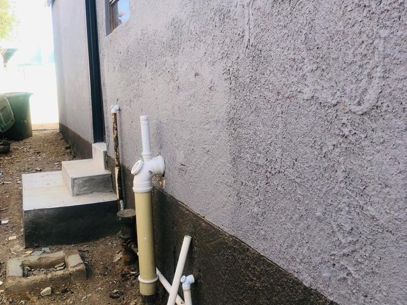 Side view of the property exterior showing exposed plumbing infrastructure, concrete steps, and textured wall finish.