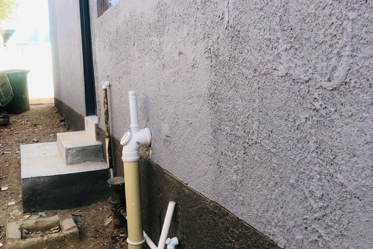 Side view of the property exterior showing exposed plumbing infrastructure, concrete steps, and textured wall finish.