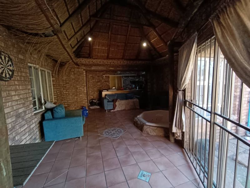 Spacious covered patio area featuring a thatched roof, exposed brick walls, tiled flooring, and a built-in spa bath.