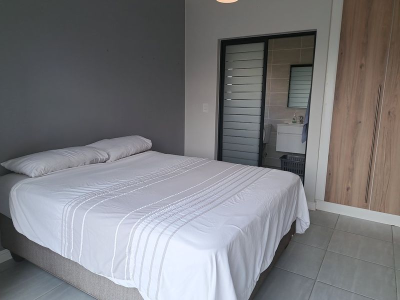 A modern bedroom featuring tiled flooring, built-in wooden cupboards, and a sliding door providing access to an en-suite bathroom.