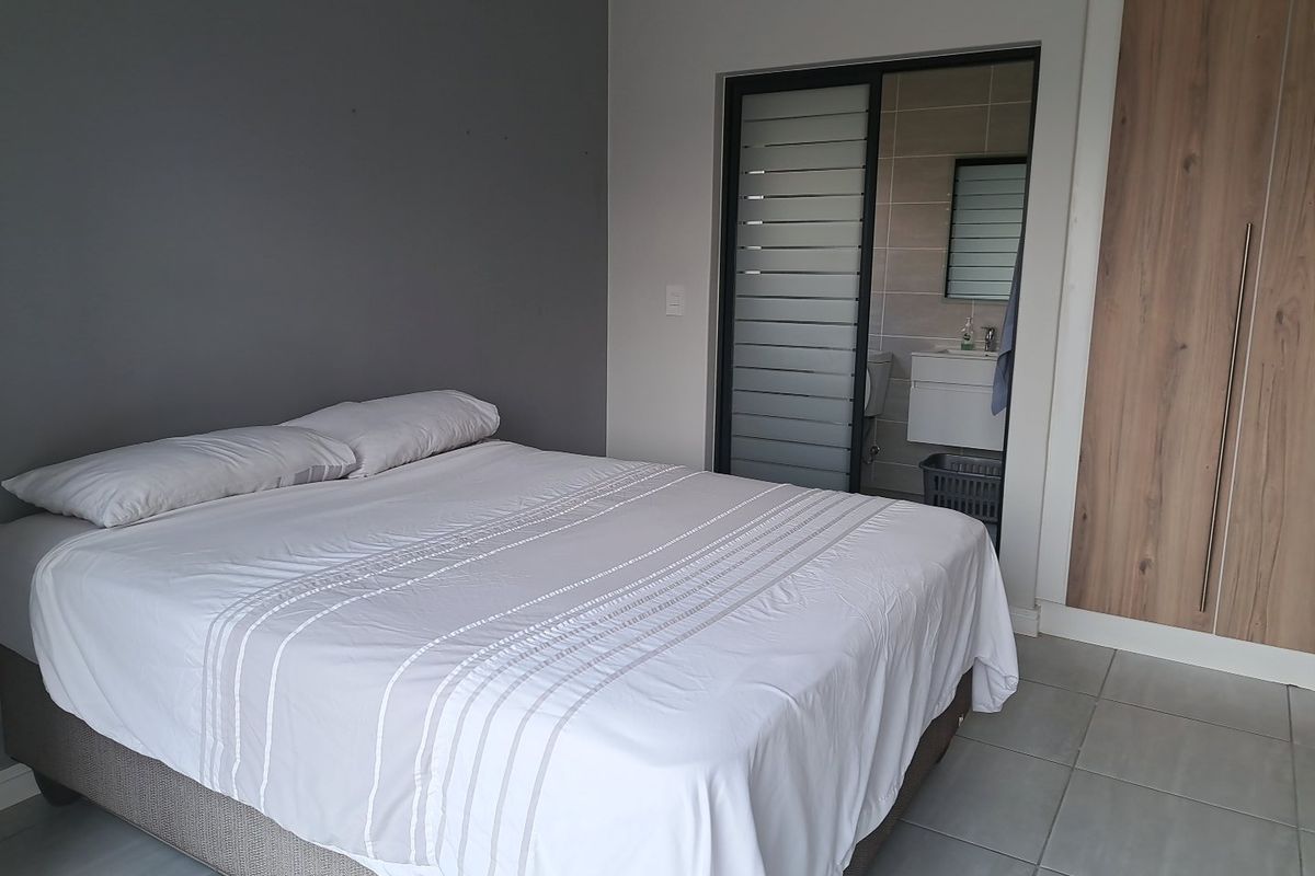A modern bedroom featuring tiled flooring, built-in wooden cupboards, and a sliding door providing access to an en-suite bathroom.