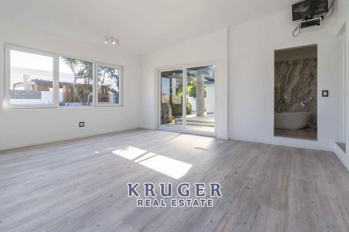 Bright living room featuring light wood-look flooring, large windows, and sliding glass doors providing direct access to the outdoor patio area.