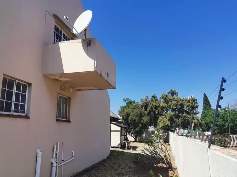 Rear exterior view of the property featuring a balcony with visible plaster damage, external plumbing, and perimeter electric fencing.