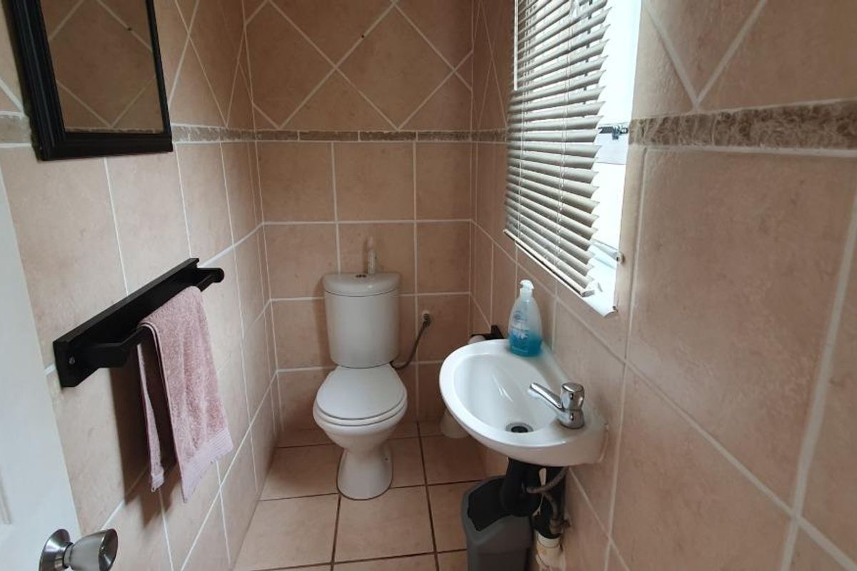 A compact guest bathroom featuring floor-to-ceiling tiling, a wall-mounted basin, and a standard toilet.