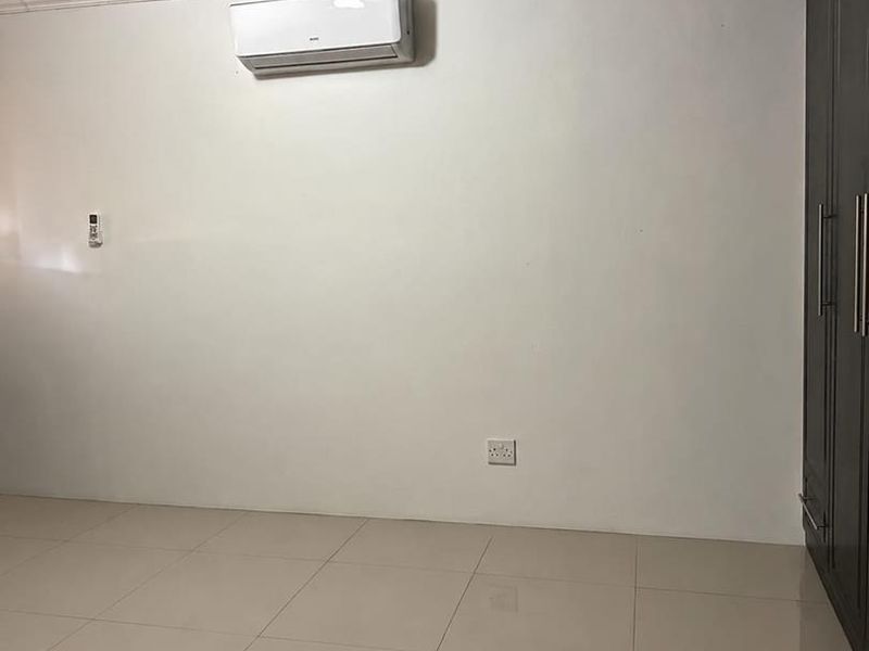 A clean, empty bedroom featuring tiled flooring, crown molding, a built-in wardrobe, and a wall-mounted split-system air conditioning unit.