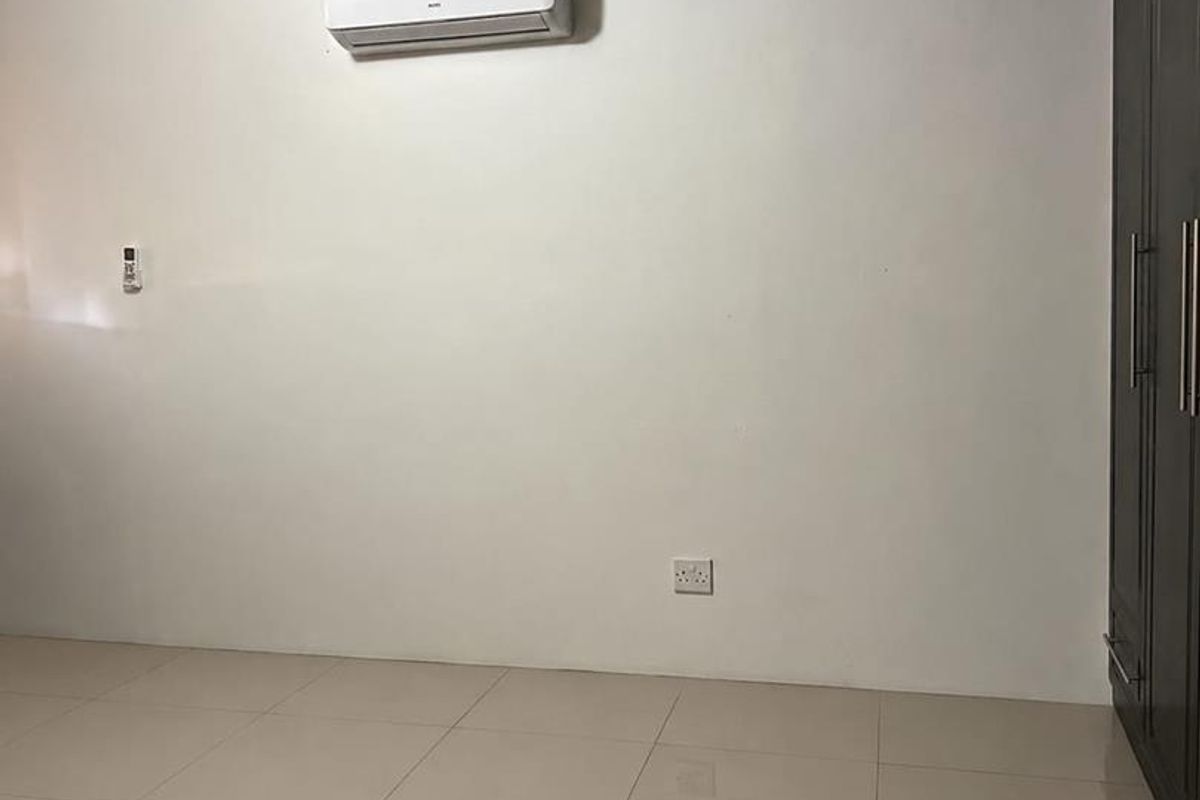 A clean, empty bedroom featuring tiled flooring, crown molding, a built-in wardrobe, and a wall-mounted split-system air conditioning unit.