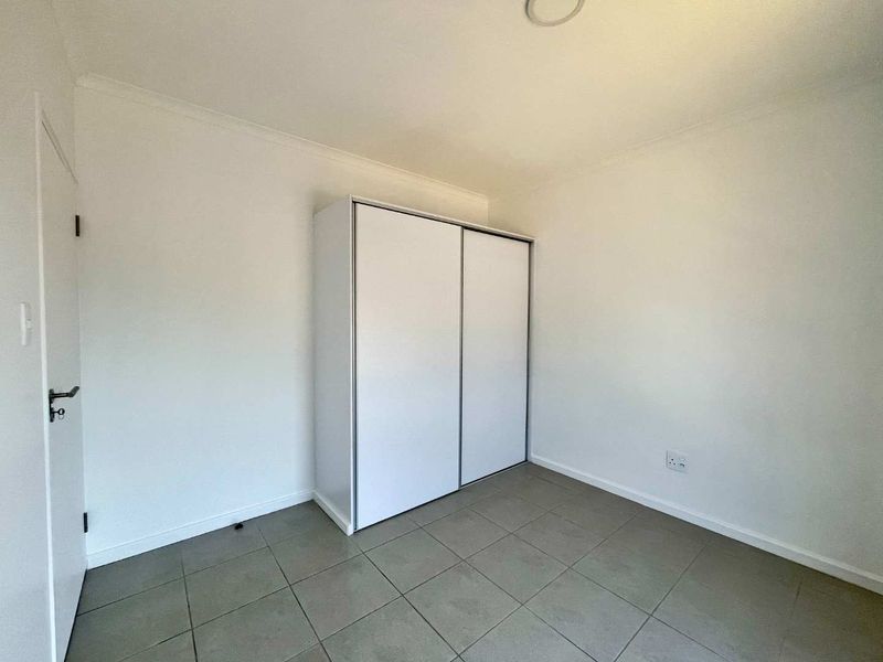 A clean, empty bedroom featuring neutral tiled flooring and a white built-in wardrobe with sliding doors.