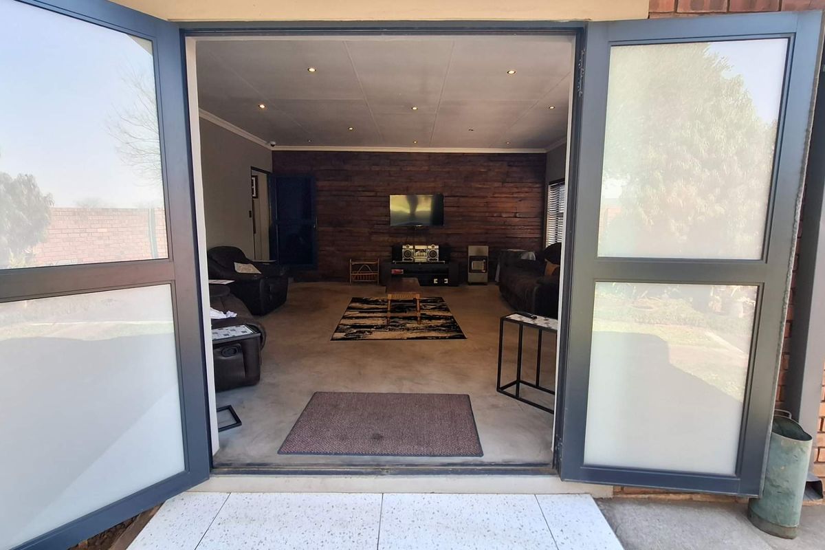 Spacious living room featuring a timber accent wall, recessed downlighting, and polished concrete floors, accessible through wide double glass doors.