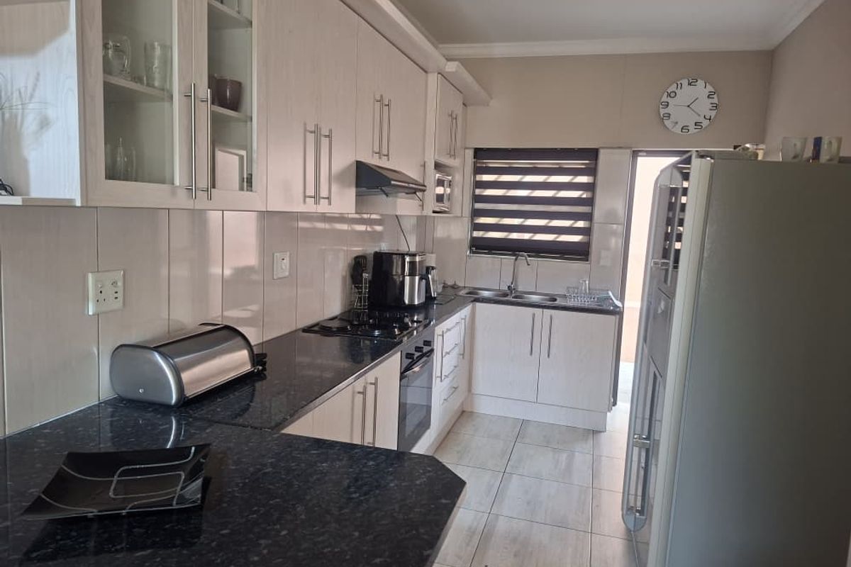 A functional kitchen featuring light wood-finish cabinetry, dark granite countertops, a built-in oven, gas hob, and an extractor fan.