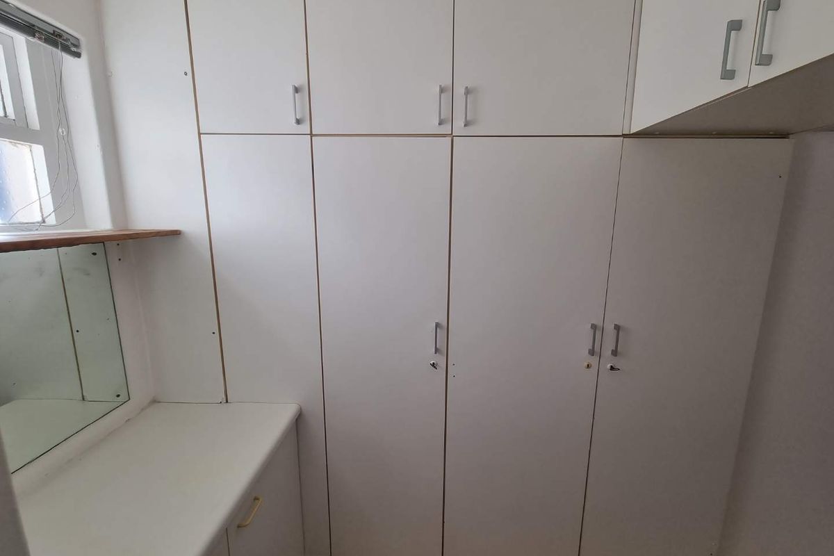 A bedroom featuring extensive white built-in cupboards with integrated vanity counter and mirror, providing ample storage space.