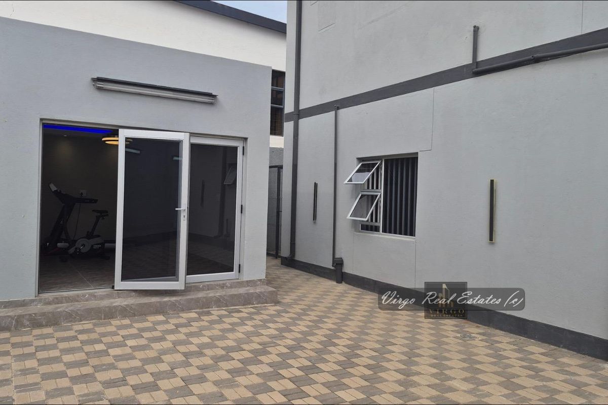 A paved rear courtyard area featuring modern grey exterior walls, aluminium sliding doors, and security-fitted windows, providing a clean and functional outdoor space.