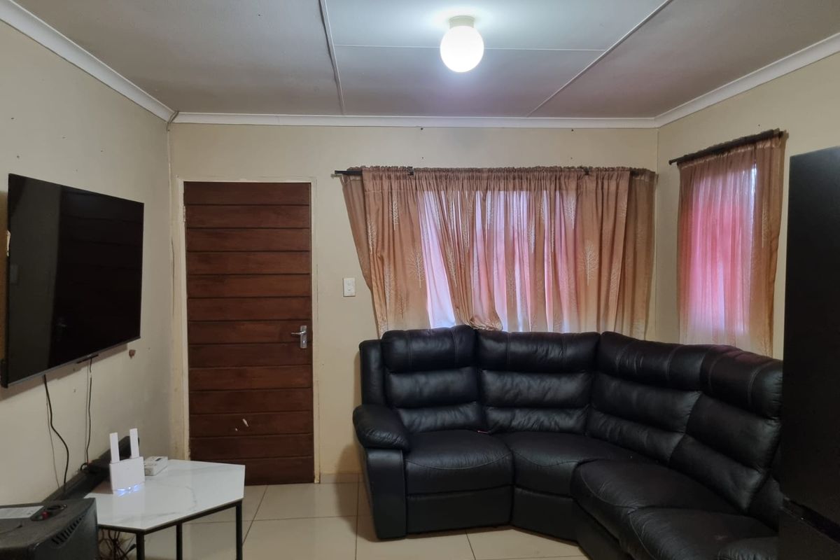 A functional living room featuring tiled flooring, a central ceiling light, and a wooden panel door, providing a neutral base for interior updates.