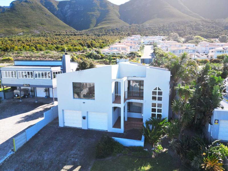 Aerial view of a modern two-story residential property featuring a double garage, paved driveway, and balcony, set against a scenic mountain backdrop.