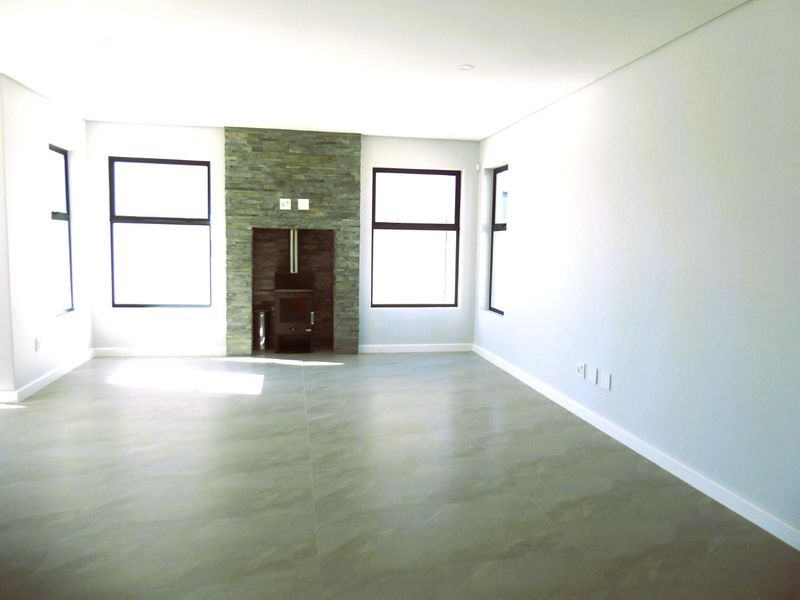 Spacious, light-filled living room featuring modern tiled flooring and a striking stone-clad fireplace with a built-in wood-burning stove.
