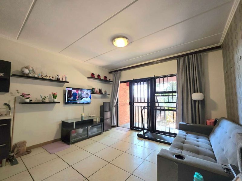 A living room featuring tiled flooring, floating wall shelves, and a sliding glass door with an integrated security gate leading to the exterior.