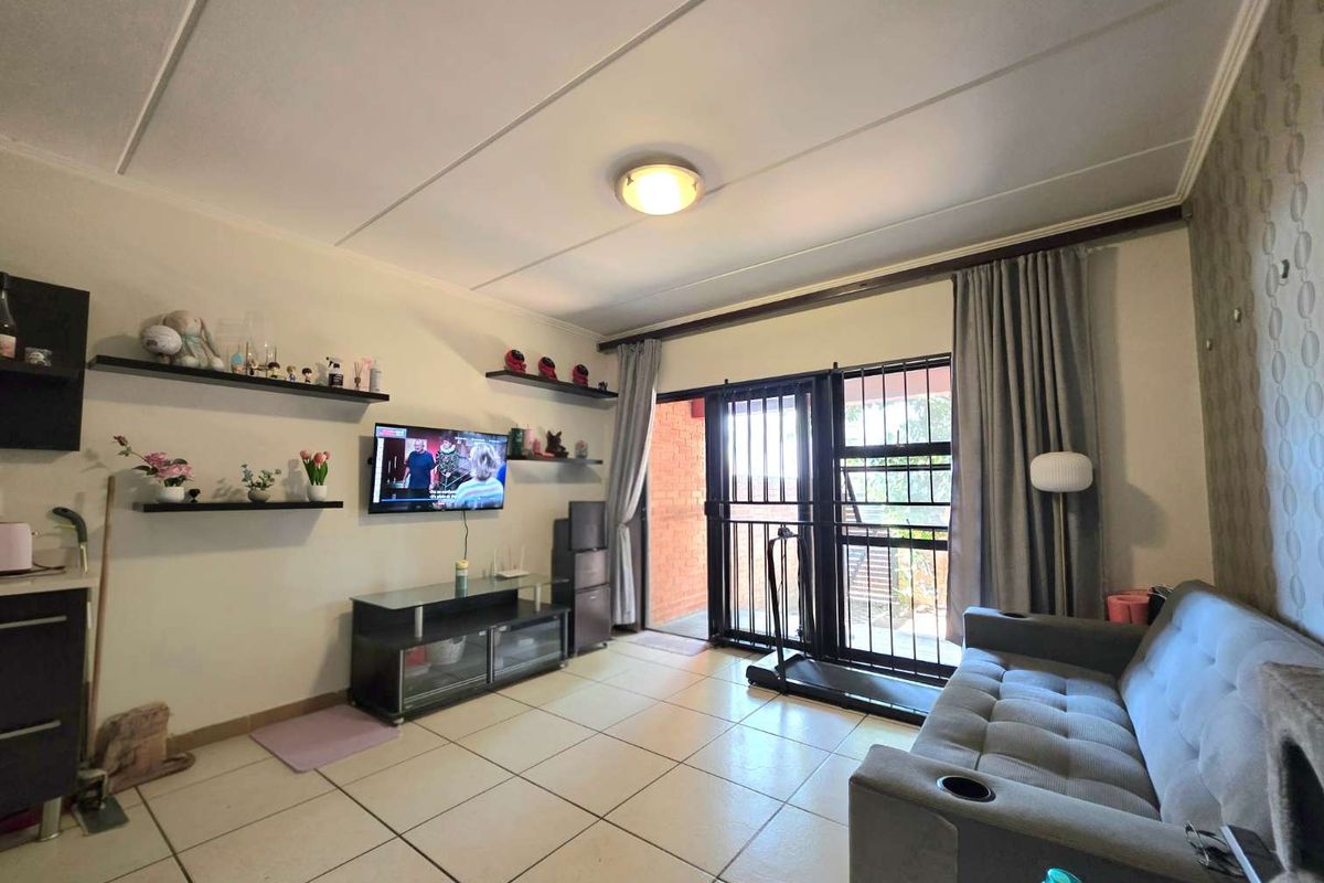A living room featuring tiled flooring, floating wall shelves, and a sliding glass door with an integrated security gate leading to the exterior.