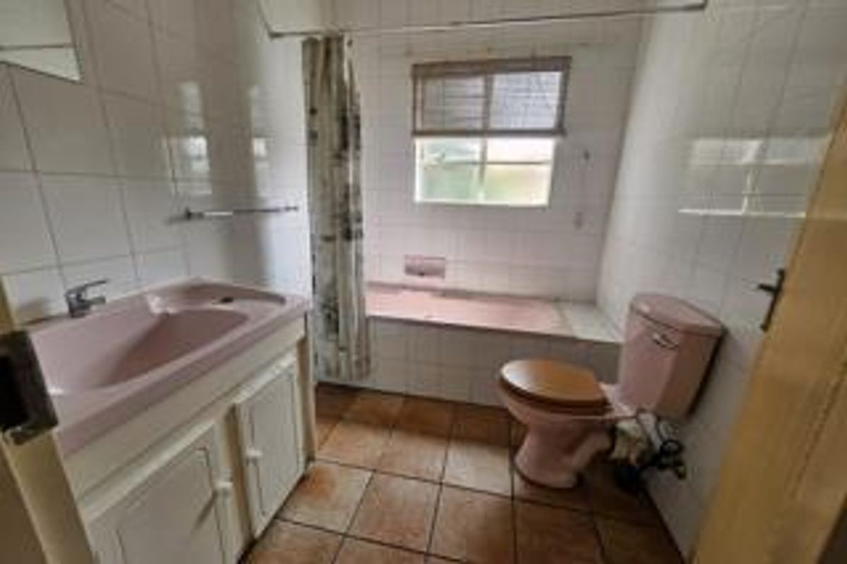 A dated bathroom featuring a pink bathtub, matching pink toilet, and a vanity basin with white cabinetry and tiled walls.