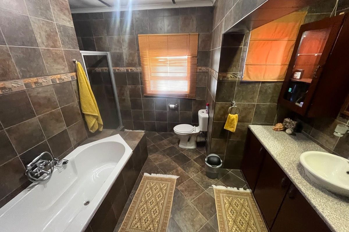 A full bathroom featuring dark tiled walls and flooring, a built-in bathtub, a separate shower enclosure, and a vanity with a vessel sink.