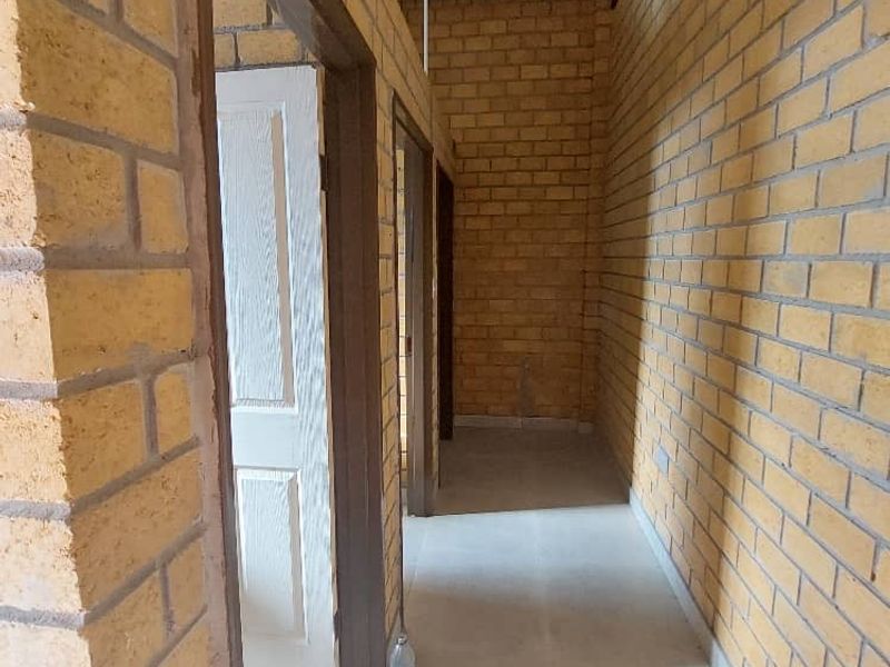 A functional hallway featuring exposed brick walls, tiled flooring, and a corrugated metal ceiling, providing access to multiple internal rooms.