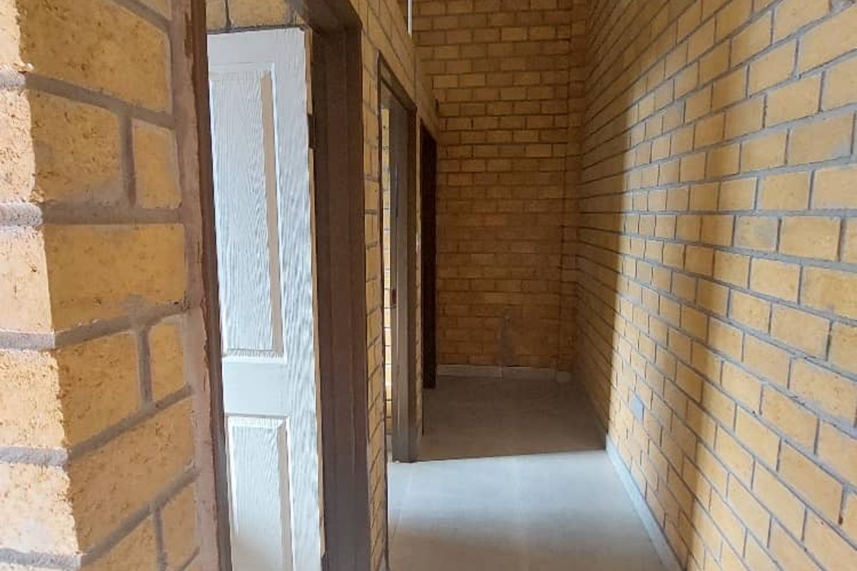 A functional hallway featuring exposed brick walls, tiled flooring, and a corrugated metal ceiling, providing access to multiple internal rooms.